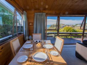 a dining room with a table and chairs and windows at Beach House on the Ridge - Kaiteriteri House in Kaiteriteri
