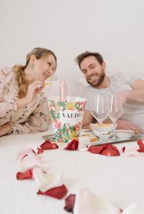 Um homem e uma mulher sentados na cama com uma mesa com taças de vinho. em Hotel Giulietta e Romeo ***S em Verona mais 116 fotografias