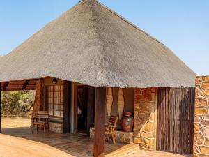 Cabaña pequeña con techo de paja, mesa y sillas en Kwalata Game Lodge, en Klipdrift