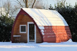 un petit hangar rouge et blanc dans la neige dans l'établissement Luxe Eco Pod op Camping de Stal, à Drijber