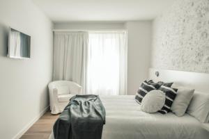 a white bedroom with a large bed and a chair at Tramuntana Hotel - Adults Only in Cadaqués
