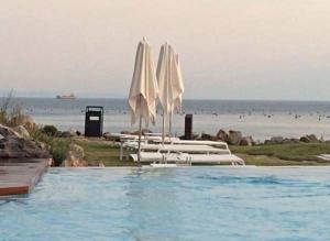 a swimming pool with white umbrellas and the beach at Portopiccolo Avolare Apartments in panoramic terrasses, beach included in Sistiana