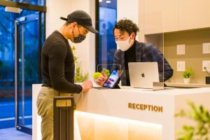 a man in a face mask standing at a reception desk at &AND HOSTEL ASAKUSA KAPPABASHI in Tokyo