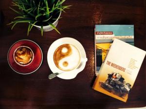 una mesa con una taza de café y un libro en U Dee Room and Coffee, en Kanchanaburi