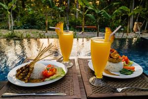 a table with plates of food and two glasses of orange juice at Alam Selumbung Garden in Nusa Penida