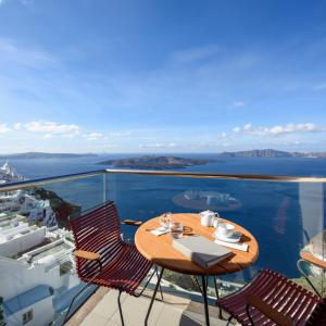 een tafel en stoelen op een balkon met uitzicht op de oceaan bij Panorama Boutique Hotel in Fira