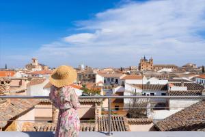 a woman in a hat standing on a balcony looking at a city at Hotel Spa La Casa del Rector Almagro in Almagro