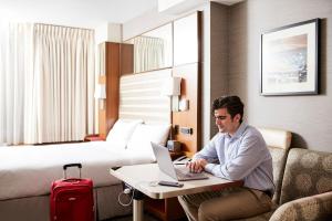un hombre sentado en un escritorio con un portátil en una habitación de hotel en Club Quarters Hotel Grand Central, New York, en Nueva York