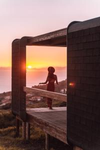 卡列塔的住宿－Calheta Glamping Pods - Nature Retreat，站在长凳上看着日落的女人