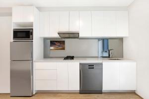 a kitchen with white cabinets and a stainless steel refrigerator at Bondi Beach Studios Suite in Sydney