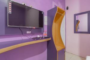 a tv on top of a purple wall with a desk at RedDoorz @ Cipanas Garut in Garut