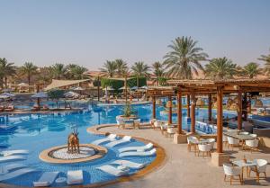 
a swimming pool with several tables and chairs at Anantara Qasr al Sarab Desert Resort in Jurayrah
