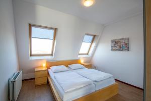 een slaapkamer met een bed met witte lakens en 2 ramen bij Duinerei appartement B301 - Groote Keeten in Callantsoog