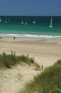 a sandy beach with boats in the water and a person walking on it at Hôtel Restaurant & Spa Plaisir in Le Bois-Plage-en-Ré