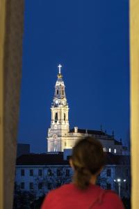 une femme debout devant un bâtiment avec une tour d'horloge dans l'établissement Hotel Santa Maria, à Fátima