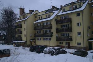 ein großes gelbes Gebäude mit Autos im Schnee in der Unterkunft Kinapp Stay in Szklarska Poręba