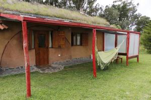 una hamaca frente a una casa con techo de hierba en Alojamiento Ecológico Kurache en Tandil