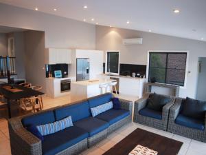 a living room with a blue couch and a kitchen at Beachside Holiday Home with Stunning Seaviews in Avoca Beach