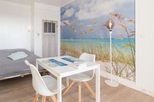 1 dormitorio con una mesa y sillas blancas y un mural de playa en Studio Le Lavandou, en De Panne