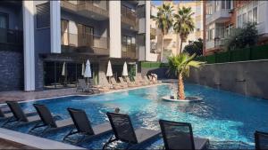 a swimming pool with chairs and a palm tree in front of a building at C-LOUNGE CLEOPATRA APAPRTMENT in Alanya