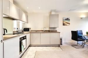 cocina con armarios blancos, mesa y sillas en Sapphire Serviced Apartment en Chelmsford