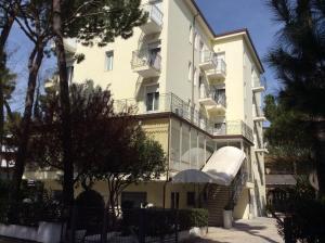 a large white building with a balcony and trees at Hotel Augustus in Milano Marittima