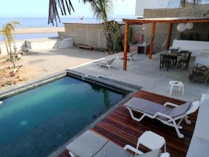 a swimming pool with chairs and a table and the beach at Hotel Navego in Lobitos