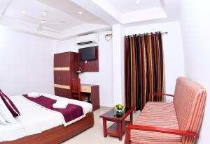 a bedroom with a bed and a chair and a television at Puthens Capitol Inn in Cochin