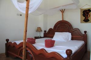 una cama de madera con sábanas blancas y almohadas rojas. en HOMELAND SWAHILI LODGE Nungwi Backpacker Apartments BUDGET en Nungwi