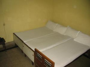 Ce lit se trouve dans un dortoir doté de draps et d'oreillers blancs. dans l'établissement Vasantha Lodge Purasawalkam chennai, à Chennai
