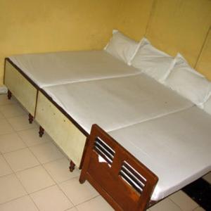 un letto bianco con struttura in legno in una stanza di Vasantha Lodge Purasawalkam chennai a Chennai