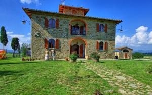 a large stone house with red windows on a green field at Villa Eleonora in Lucignano