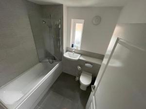 a bathroom with a tub and a toilet and a sink at Modern Room With Huge Bed - Walk to City Centre! in Manchester