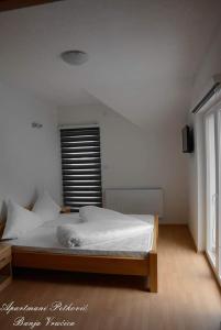 a bedroom with a bed with white sheets and a window at APARTMANI PETKOVIC in Teslić