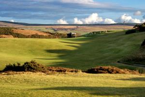 a green golf course with a barn in the distance at Kinloch Hotel, Isle of Arran in Blackwaterfoot