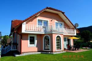 a pink house with a balcony and a table at Vila Deluxe & Apartmány Riviéra Liptov Bešeňová in Bešeňová