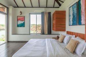 a bedroom with a large white bed with two windows at Casa Paun by StayVista - A lake-view villa with Infinity pool, Modern interiors & an amphitheatre in Nethersole Dam +28 photos