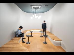 横浜市にあるカプセルプラス横浜 サウナ&カプセルの二人の男性がテーブルとスツールを備えた部屋に座っている