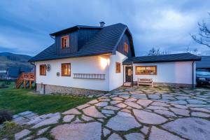 a white house with a black roof and a stone driveway at Chalupa Pri Grúni in Zázrivá