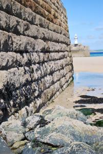 a brick wall next to a beach with a lighthouse at The Western in St Ives
