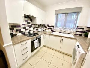 a white kitchen with black and white tiles on the wall at EasyRest Spalding - 4 Beds & Free Parking - Central & Modern Open Plan Apartment - Convenient Location in Spalding