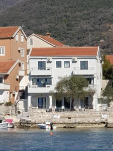 una grande casa bianca sull'acqua accanto agli edifici di Beach Apartments a Tivat