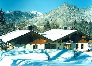una casa cubierta de nieve con montañas en el fondo en Forsthaus Röthelmoos inkl. Chiemgaukarte, en Ruhpolding