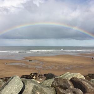 a rainbow over a beach with rocks and the ocean at High Tide in Whitby