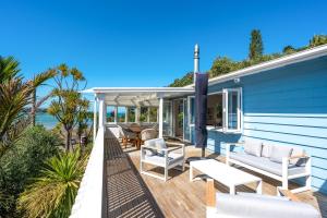 a deck with white furniture on a blue house at Bluebelle in Oneroa
