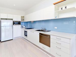 a white kitchen with a sink and a refrigerator at Comfy Beachfront Unit, Unbeatable Location & Views in Avoca Beach