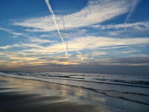 a jet contrail in the sky over the beach at Tamar 2 in Katwijk aan Zee
