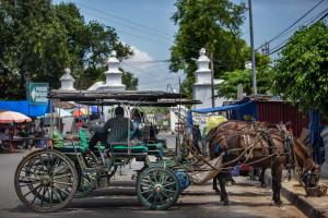 a horse pulling a horse drawn carriage down a street at Amaris Hotel Malioboro - Jogja in Yogyakarta