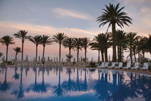 una piscina con palmeras y tumbonas en Hotel Riu Palace Tres Islas, en Corralejo