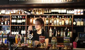 a woman behind a bar with a bottle of alcohol at The Fountaine Inn in Linton